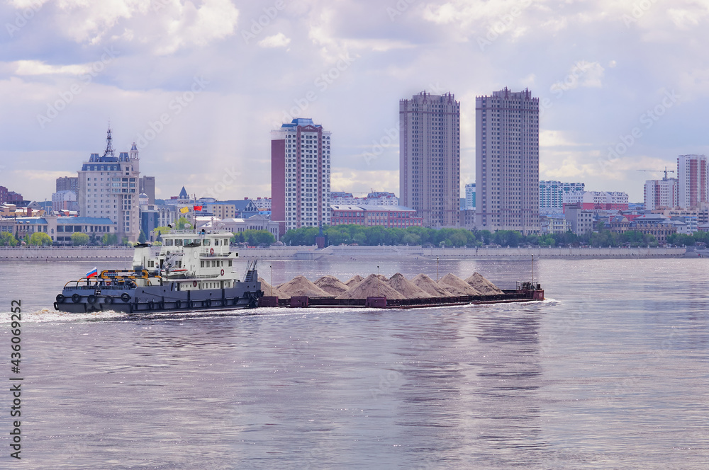 A barge loaded with sand moves along the Amur River. In the background is the city of Heihe, China. View from the embankment of the city of Blagoveshchensk, Russia.