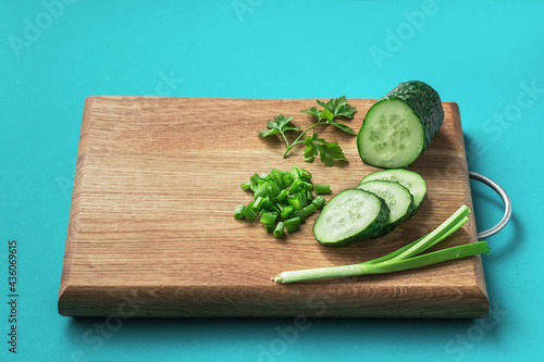Fresh chopped cucumbers and green onions on a wooden cutting board on a bright blue background with copy space.Food background.