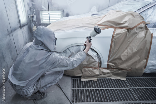 Car painting and automobile repair service. Auto mechanic in white overalls paints car with airbrush pulverizer in paint chamber.