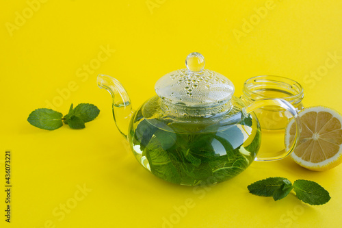 Mint tea in the glass teapot, lemon and honey on the yellow background. Close-up. Copy space.