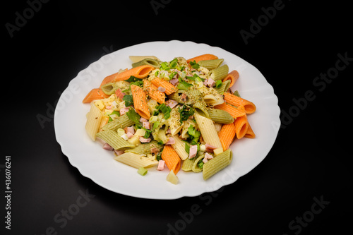 serving of colored penne pasta with tomato sauce, ham and basil