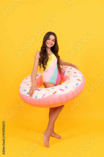 happy kid in swimming suit with doughnut inflatable ring on yellow background, childhood.