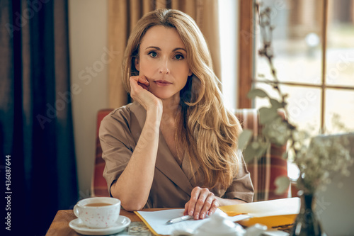 Blonde long-haired woman sitting at the table and looking thoughtful