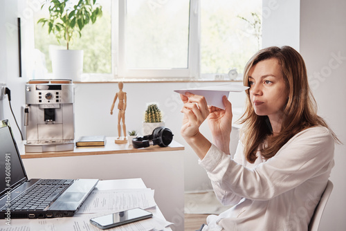 Woman procrastinate at workplace. Freelancer on remote work at home office. Unmotivated tired woman play with paper plain. Lazy office worker