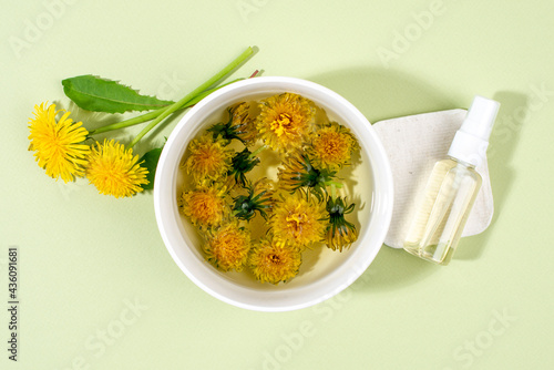 Dandelions (Taraxacum) in a bowl with boiling water and spray bottle with face toner. Home made beauty product. photo