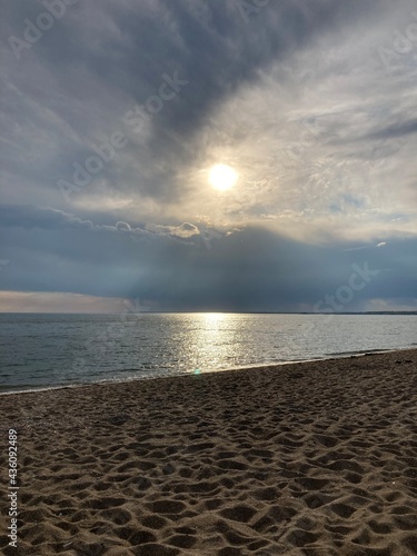 Sandy beach with peering sun through the evening clouds