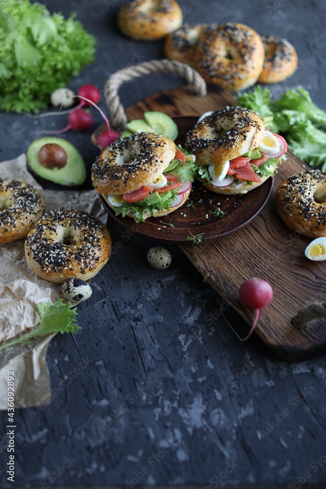 Bagels with salmon, avocado and green lettuce on a wooden board. Breakfast with light healthy snacks. Bagels with salmon, avocado and green lettuce on a wooden board. Breakfast with light healthy snacks.