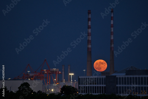 Beautiful view of red super flower Moon rise in the Irish sky between iconic Poolbeg Generating Station (Poolbeg CCGT) chimneys on May 26, 2021 seen from Dublin City Motocross Track, Dublin, Ireland