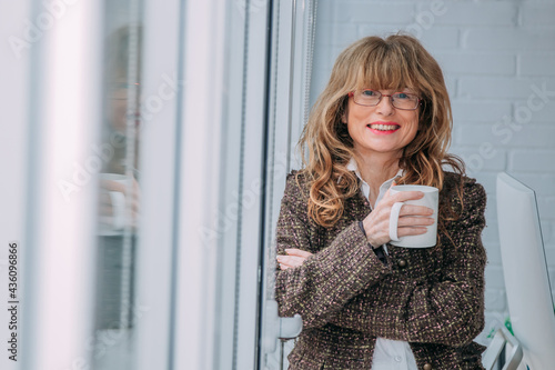 business woman in office with cup of coffee standing at window