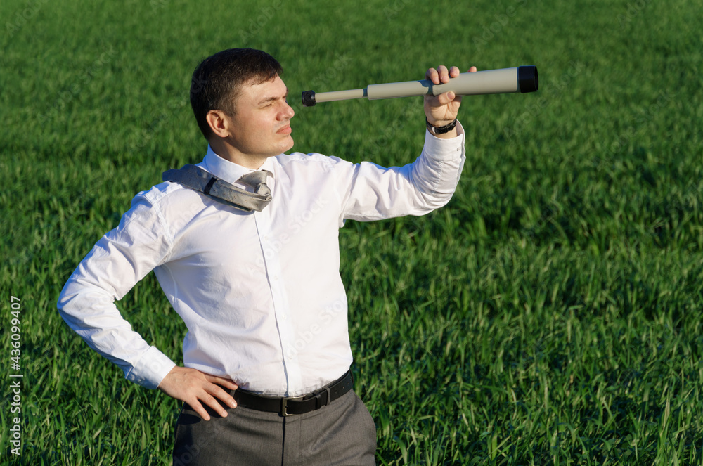 businessman poses with a spyglass, he looks into the distance and looks for something, green grass and blue sky as background businessman poses with a spyglass, he looks into the distance and looks for something, green grass and blue sky as background