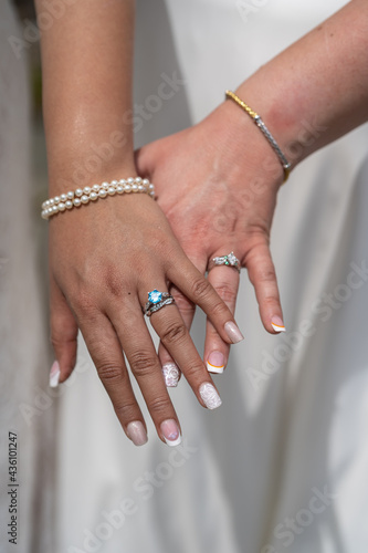 The left hands of two brides showing off their engagement and wedding rings on their wedding day. They also did their nails and wear other jewelry to accent the rings. photo