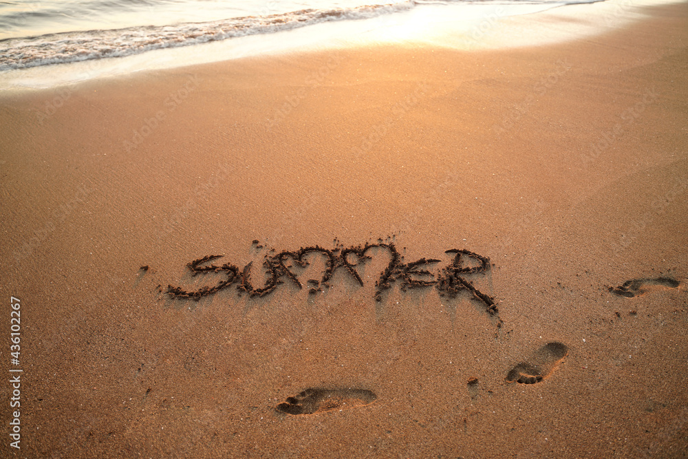 Obraz premium Text summer written on the sand in a beach. Sunset time.