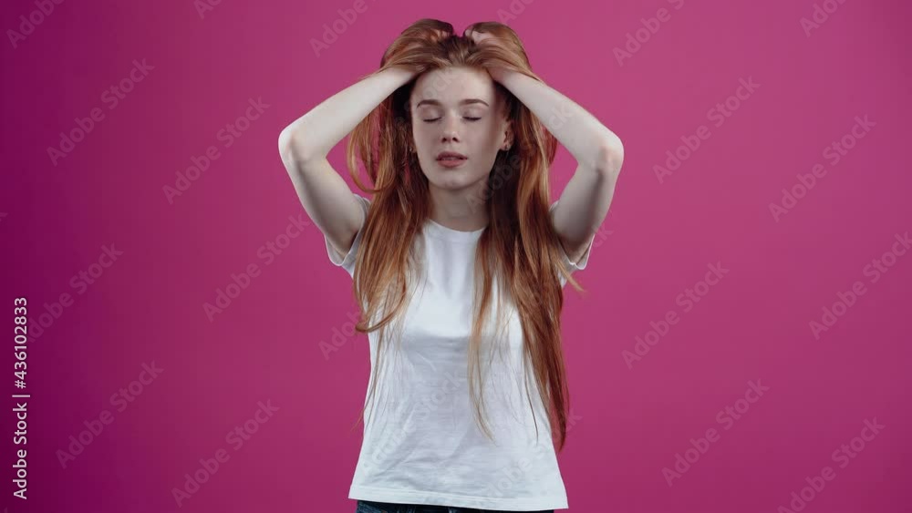 Portrait of a tired girl who worries with her hands on her head and clings to her temples. Freckled teenager in a white T-shirt, isolated on a pink background. The concept of people's lifestyle Portrait of a tired girl who worries with her hands on her head and clings to her temples. Freckled teenager in a white T-shirt, isolated on a pink background. The concept of people's lifestyle