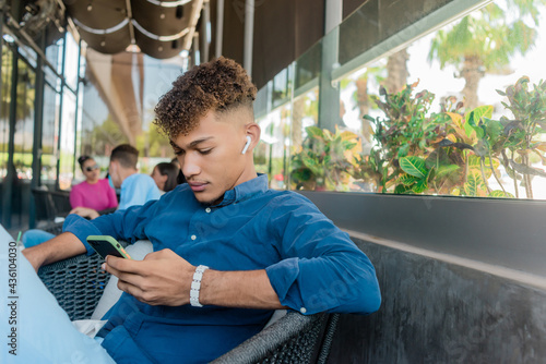 Joven latino escuchando musica y escribiendo en el celular sentado en el sof√°.