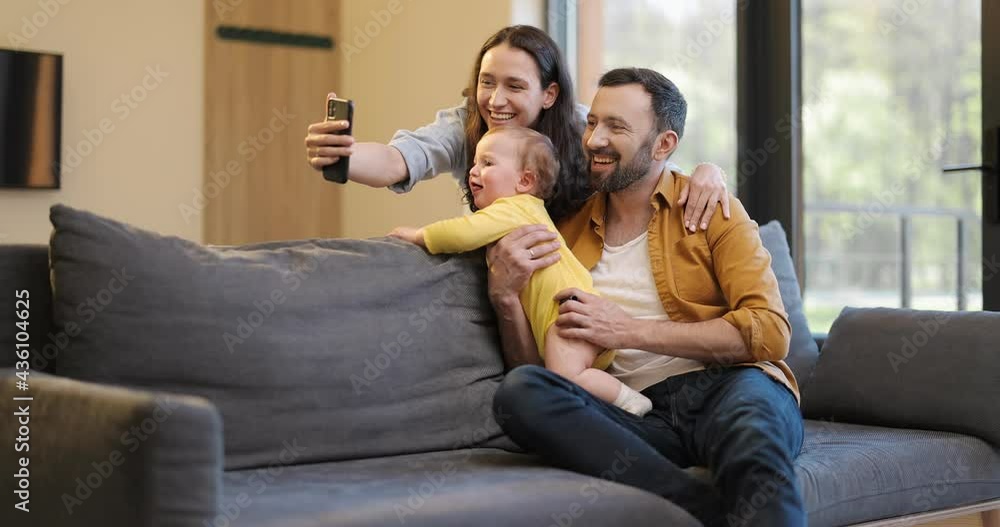 Happy family with a one year baby boy having a video call on phone from home. Concept of remote family communication on mobile devices during pandemic Happy family with a one year baby boy having a video call on phone from home. Concept of remote family communication on mobile devices during pandemic