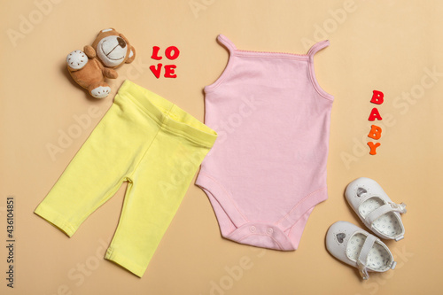 Flat Lay mockup of pink baby shirt, yellow pants, white shoes with toys on a colored background. Layout for design and placement of logos, advertising.