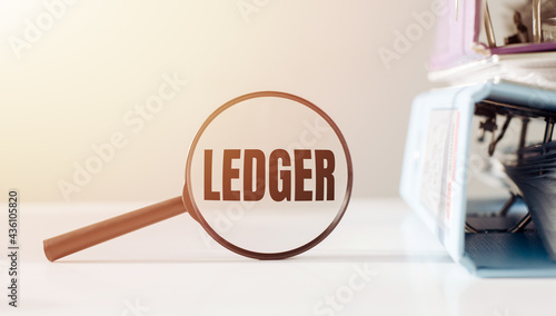 Magnifying glass with the word LEDGER on office table.