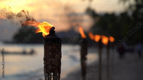 Flame form tiki torch at sunset with silhouette of palm tree in slow motion. Vacation and travel concept.