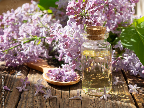 Spa oil with lilac flowers. A bottle with aromatic oil and lilac flowers on a wooden background.copy space