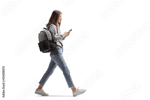 Full length profile shot of a female student walking with a mobile phone