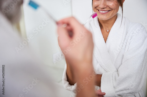 Elegant woman in white bathrobe cleaning her teeth in bathroom