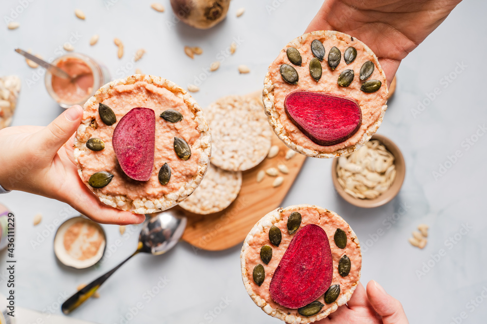 Crispy puffed rice cakes on table hummus spread and tomato and beet vegetables and sesame pumpkin seeds on the table - top view on hands holding healthy vegetarian or vegan breakfast gluten free Crispy puffed rice cakes on table hummus spread and tomato and beet vegetables and sesame pumpkin seeds on the table - top view on hands holding healthy vegetarian or vegan breakfast gluten free