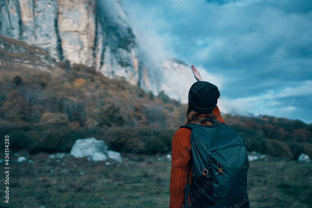 a traveler with a backpack and in a red sweater shows the mountains with her hand and the blue sky clouds a traveler with a backpack and in a red sweater shows the mountains with her hand and the blue sky clouds