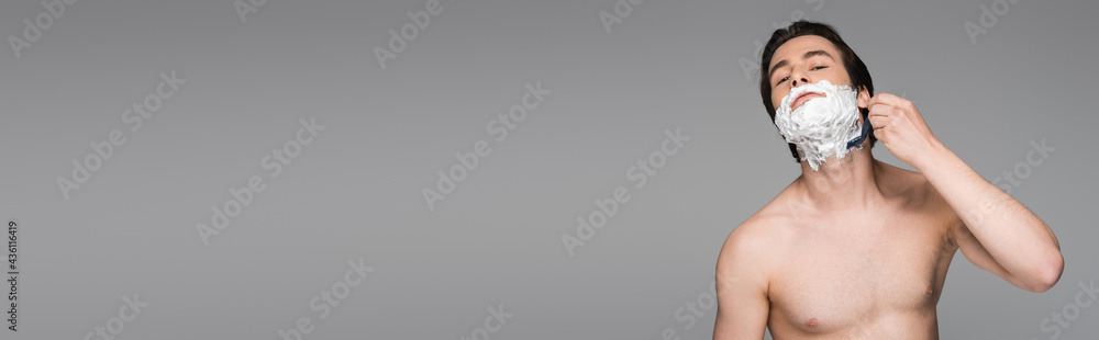 shirtless man with foam on face shaving with safety razor isolated on grey, banner.