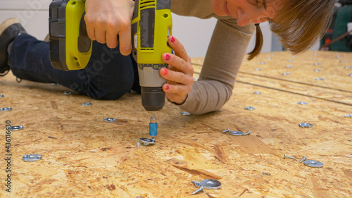Plakat w ramie CLOSE UP: Female worker screwing thin metal discs in place on a plywood panel.