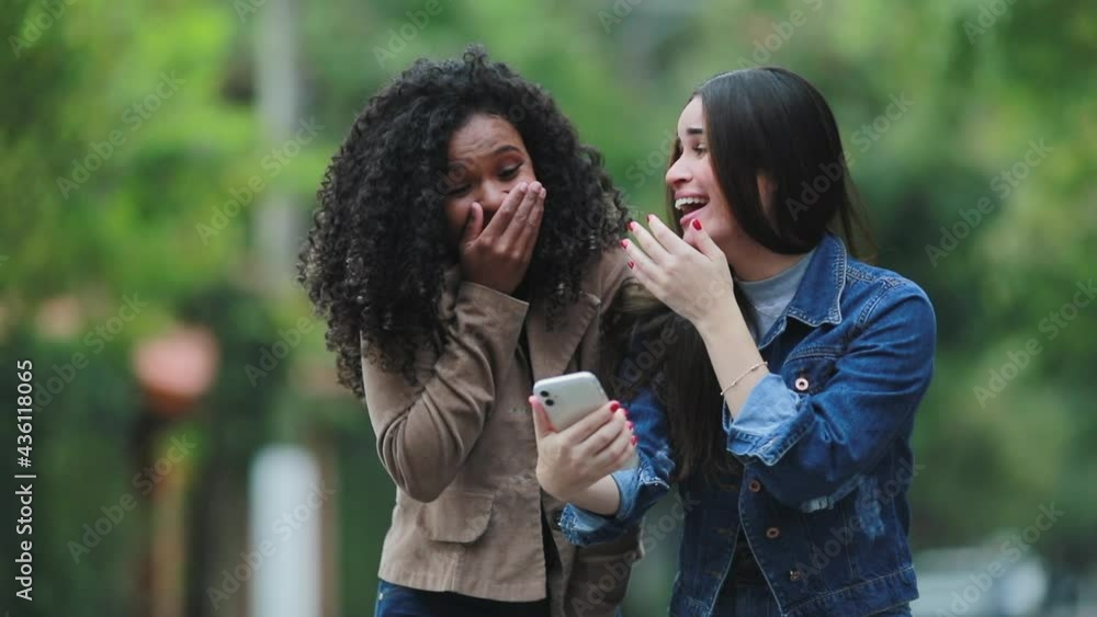 Two young women laughing and smiling at cellphone media together. Two young women laughing and smiling at cellphone media together.