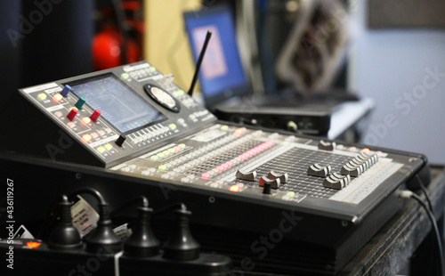 A small sound engineering studio mixing deck board and laptop in the background. Board with multiple lights, switches, dials and level adjustments for laying down tracks and calibrating sound.