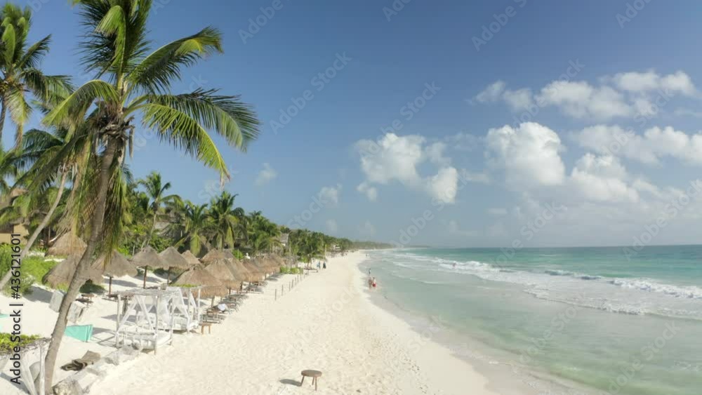 Aerial Moving Forward Along A Beautiful Caribbean Beach Resort Lined With Thatched Umbrellas, Lounge Chairs, Lapping Waves, And Soaring Palm Trees Under A Bright Blue Sky - Tulum, Mexico Aerial Moving Forward Along A Beautiful Caribbean Beach Resort Lined With Thatched Umbrellas, Lounge Chairs, Lapping Waves, And Soaring Palm Trees Under A Bright Blue Sky - Tulum, Mexico
