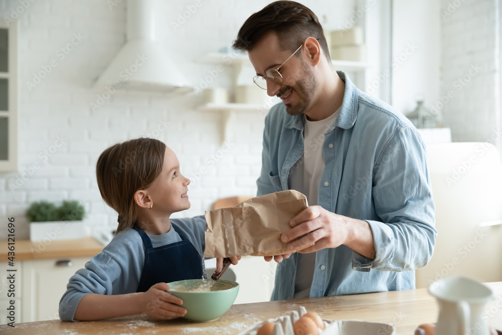 Happy loving young Caucasian father teach small 7s daughter baking preparing dough in kitchen together. Smiling caring dad and little girl child cook at home sweet cookies or pie. Parenthood concept. Happy loving young Caucasian father teach small 7s daughter baking preparing dough in kitchen together. Smiling caring dad and little girl child cook at home sweet cookies or pie. Parenthood concept.