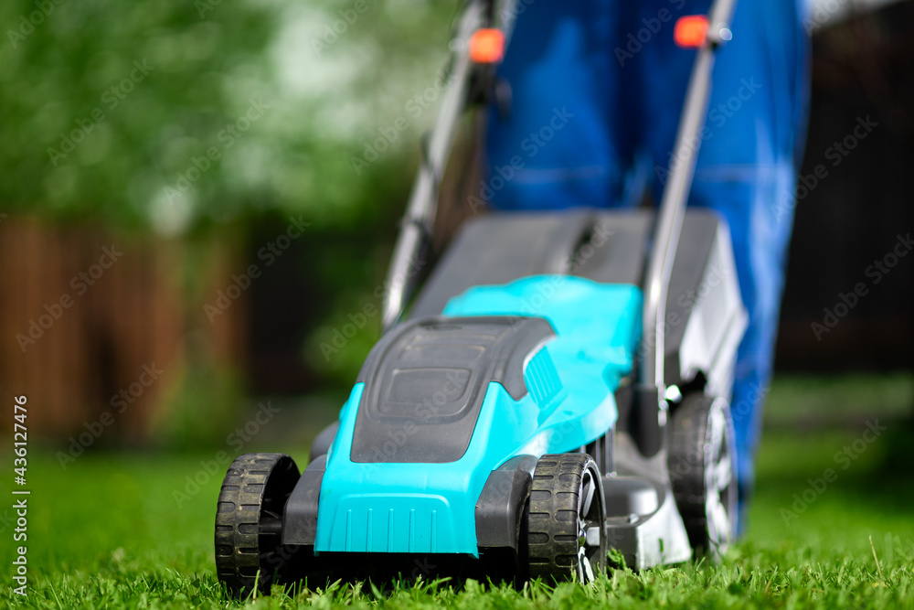 Close-up of a man in overalls with a lawn mower cutting green grass in a modern garden. Lawn mowing machine. Close-up of a man in overalls with a lawn mower cutting green grass in a modern garden. Lawn mowing machine.