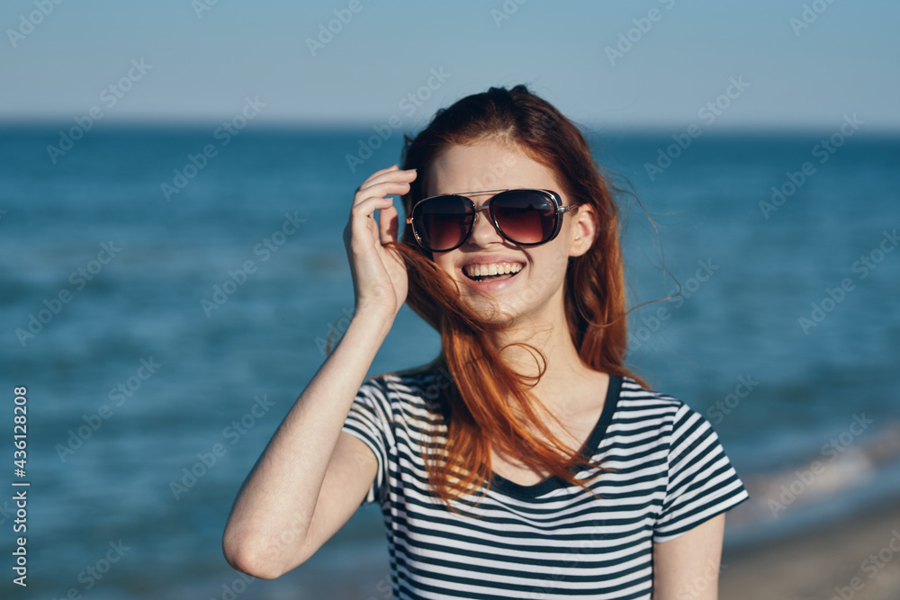 beautiful woman in sunglasses by the sea in the mountains red hair striped t-shirt beautiful woman in sunglasses by the sea in the mountains red hair striped t-shirt