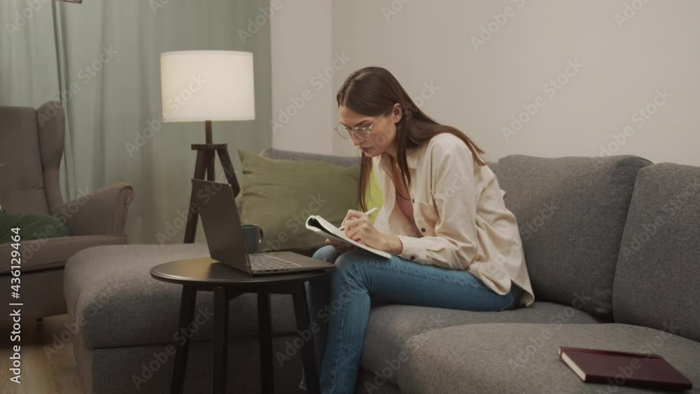 A european girl writes something in a notebook from a laptop A european girl writes something in a notebook from a laptop