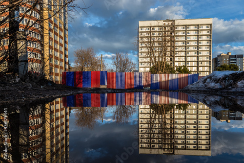 a huge puddle reflects a multi-storey building under construction fenced with a corrugated board