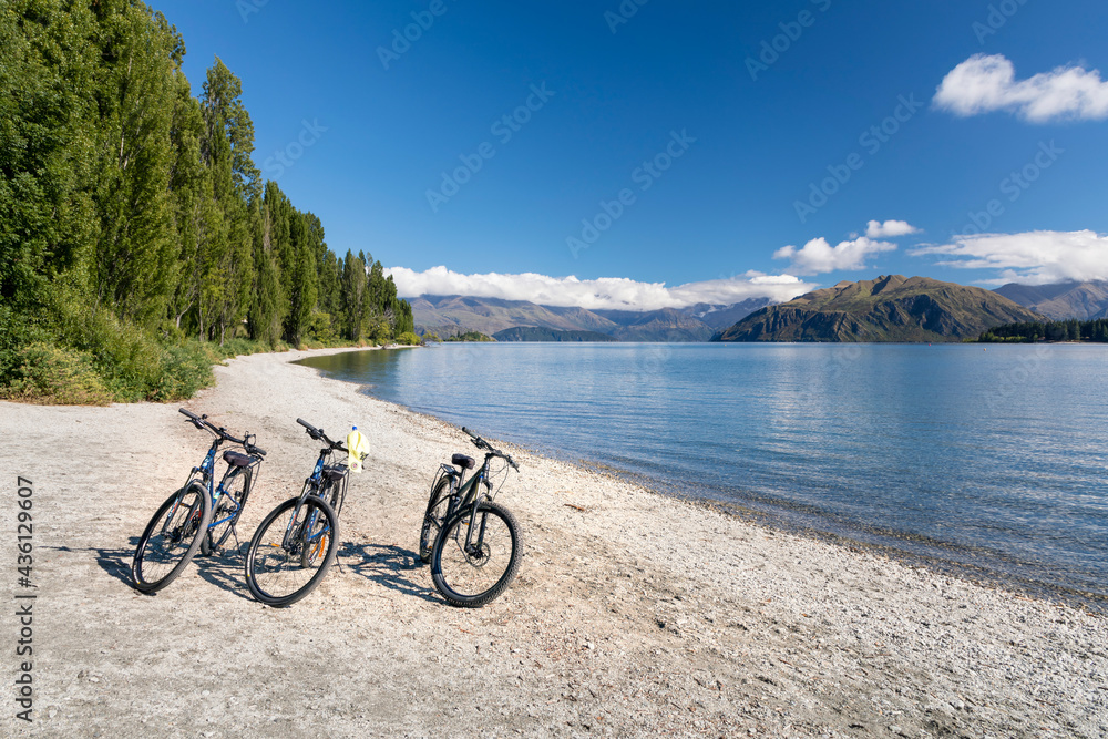 Panoramic view of Lake Wanaka bank with beach covered with white pebbles, bicycles parked near the water, South Island, New Zealand 