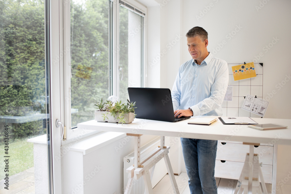 handsome businessman with blue shirt works at high table and is writing something on his black laptop handsome businessman with blue shirt works at high table and is writing something on his black laptop