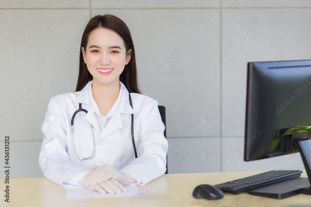 Asian professionall young smiling woman doctor sitting in office at hospital. On table has a paper and computer. Asian professionall young smiling woman doctor sitting in office at hospital. On table has a paper and computer.