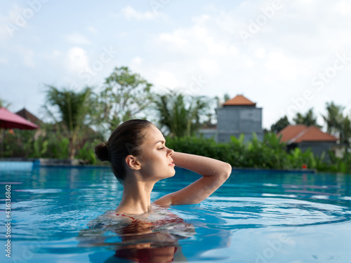 woman with bare shoulders Swims in the pool and tall trees summer vacation model
