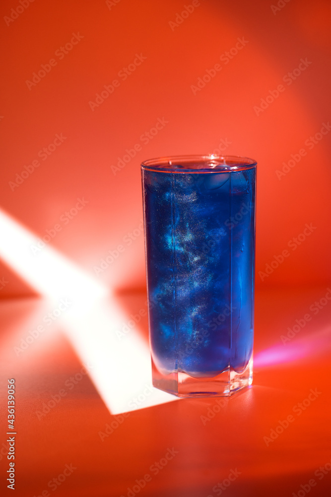 Closeup vertical image of blue cocktail with shimmer shining at red minimal background with spotlight Closeup vertical image of blue cocktail with shimmer shining at red minimal background with spotlight