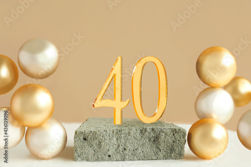 Number 40 on a concrete podium and volumetric golden balls on a beige background. Copy space..
