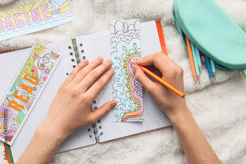 Woman coloring bookmark on bed