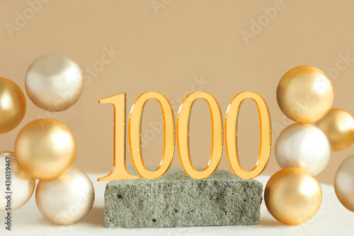 Number 1000 on a concrete podium and volumetric golden balls on a beige background. Copy space..