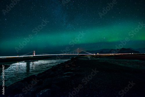 night photography of a landscape of a bridge over a river with cars crossing and with an aurora borealis on top