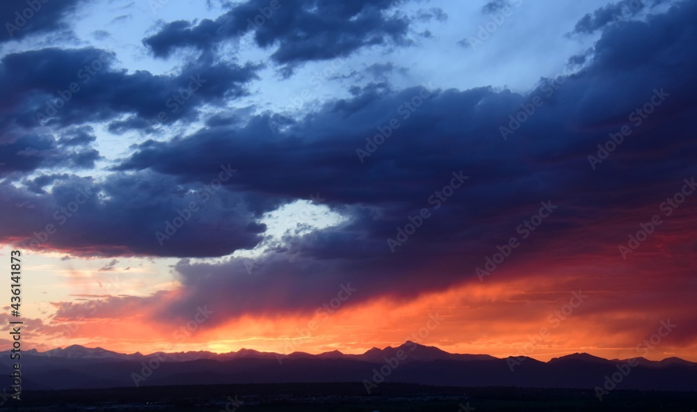 colorful ,dramatic sunset and dark clouds over long's peak and the front range of the colorado rocky mountains, as seen from broomfield, colorado