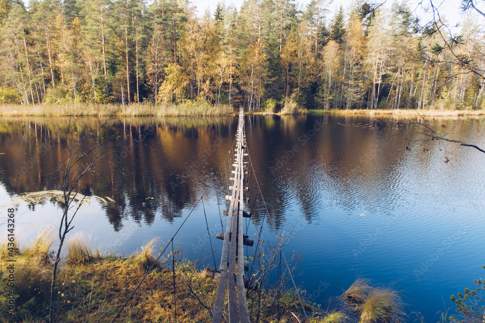 Narrow long wooden suspension bridge over the lake in Karelia, Russia. Beautiful autumn season landscape with river and forest stock photography Narrow long wooden suspension bridge over the lake in Karelia, Russia. Beautiful autumn season landscape with river and forest stock photography