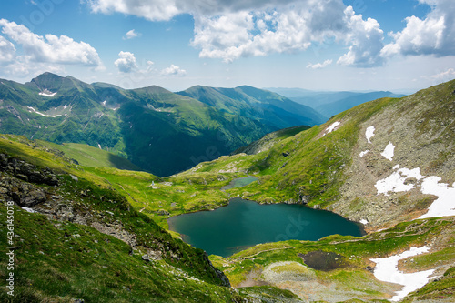 capra lake of fagaras mountains. wonderful summer nature scenery on a sunny day. popular travel destination of romania. snow and grass on the slopes. fluffy clouds on the sky