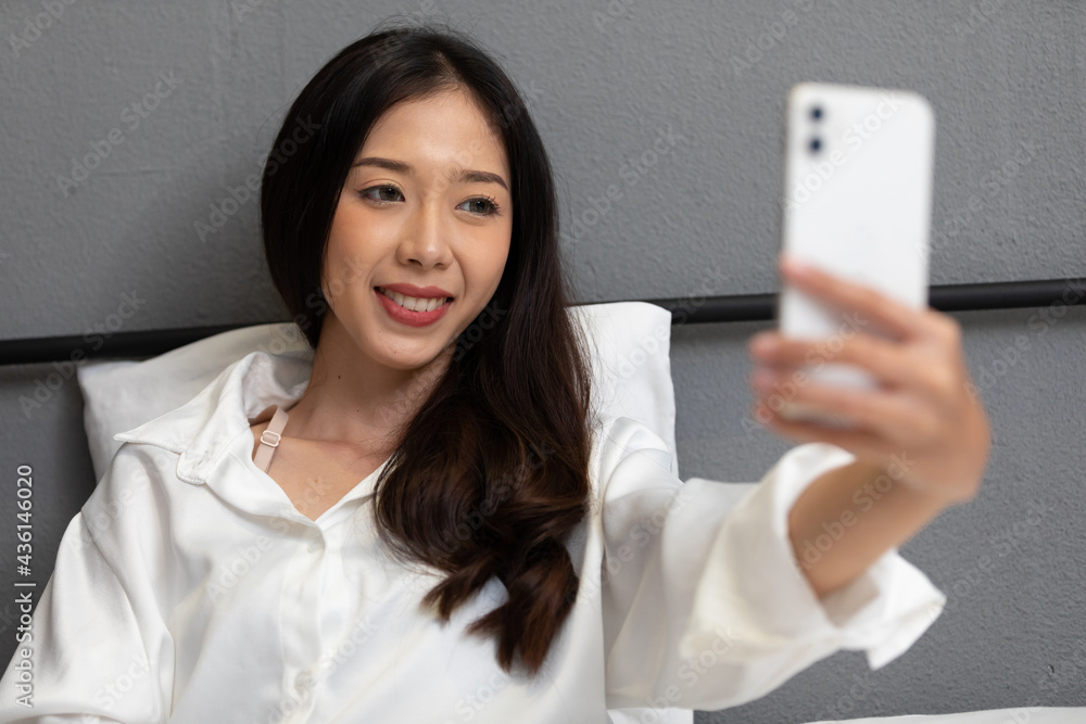young beautiful woman sitting on bed, taking photo or selfie from smartphone young beautiful woman sitting on bed, taking photo or selfie from smartphone